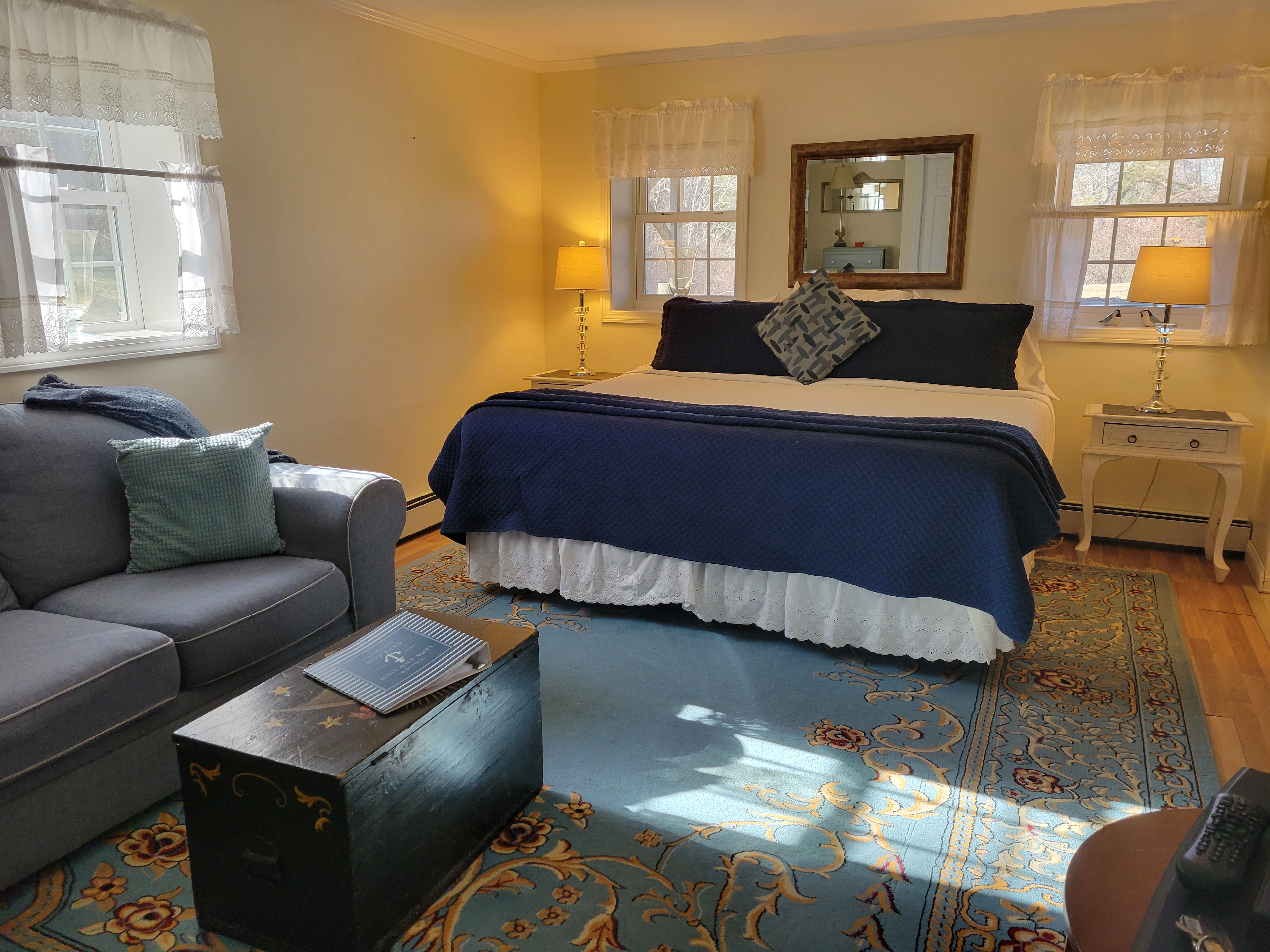 Photo of Lion's Den room with roaring wood-burning fireplace, a black chest with fresh flowers on it in front of a blue couch