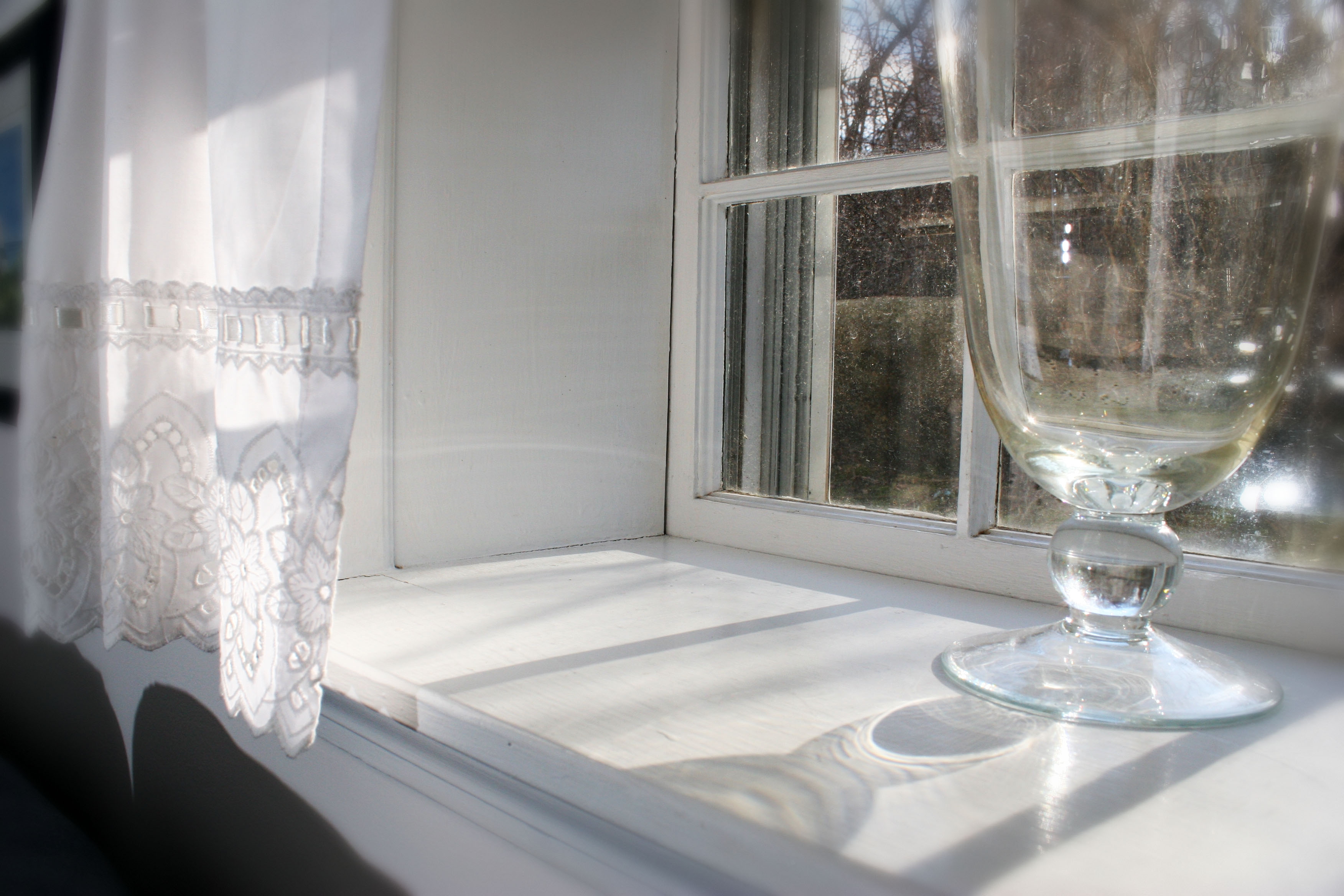 Black and white photo os a window with light streaming into it and a shiny glass vase.