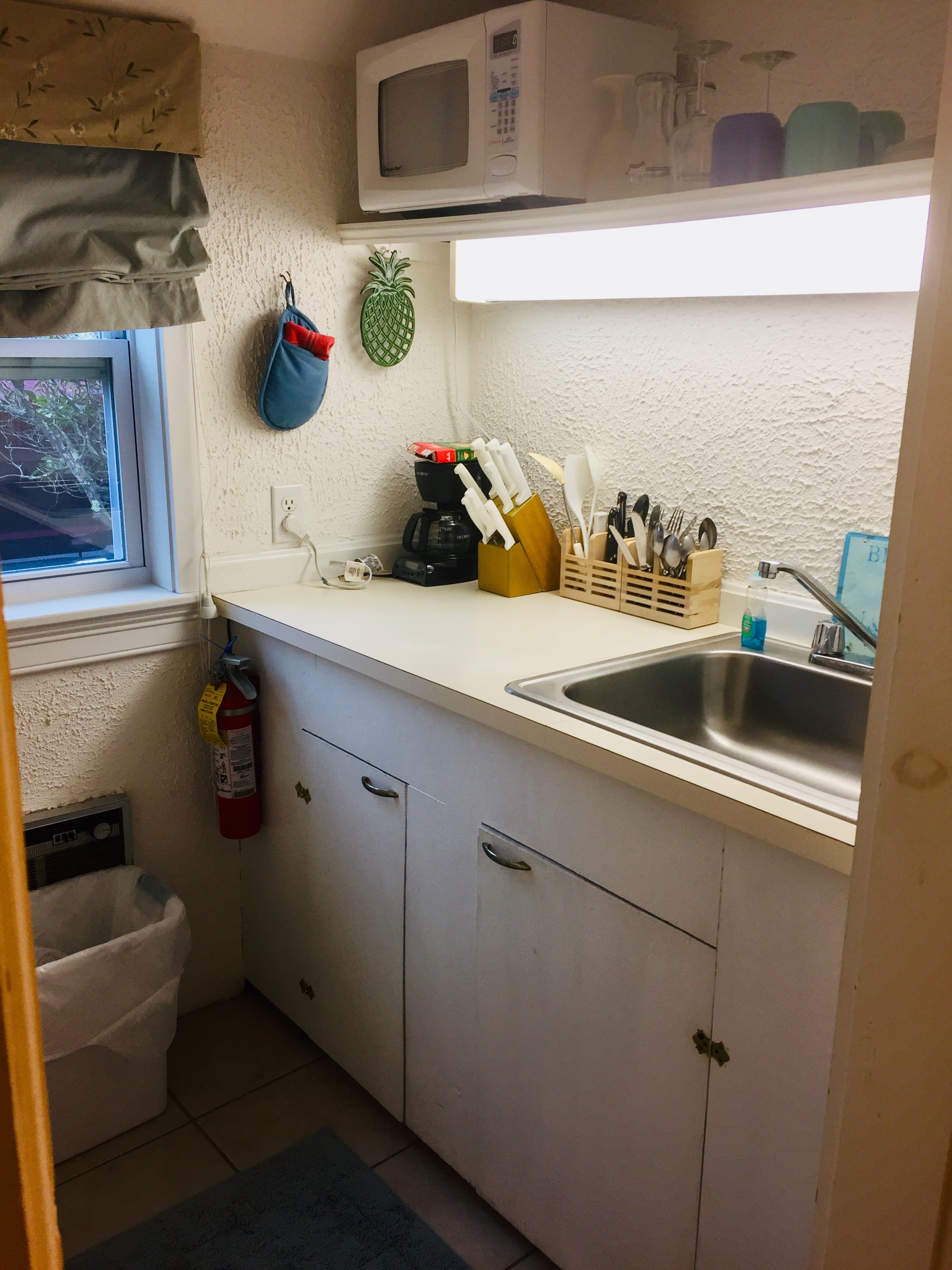 A galley kitchen with white counter top and metal sink. A microwave hangs over the window