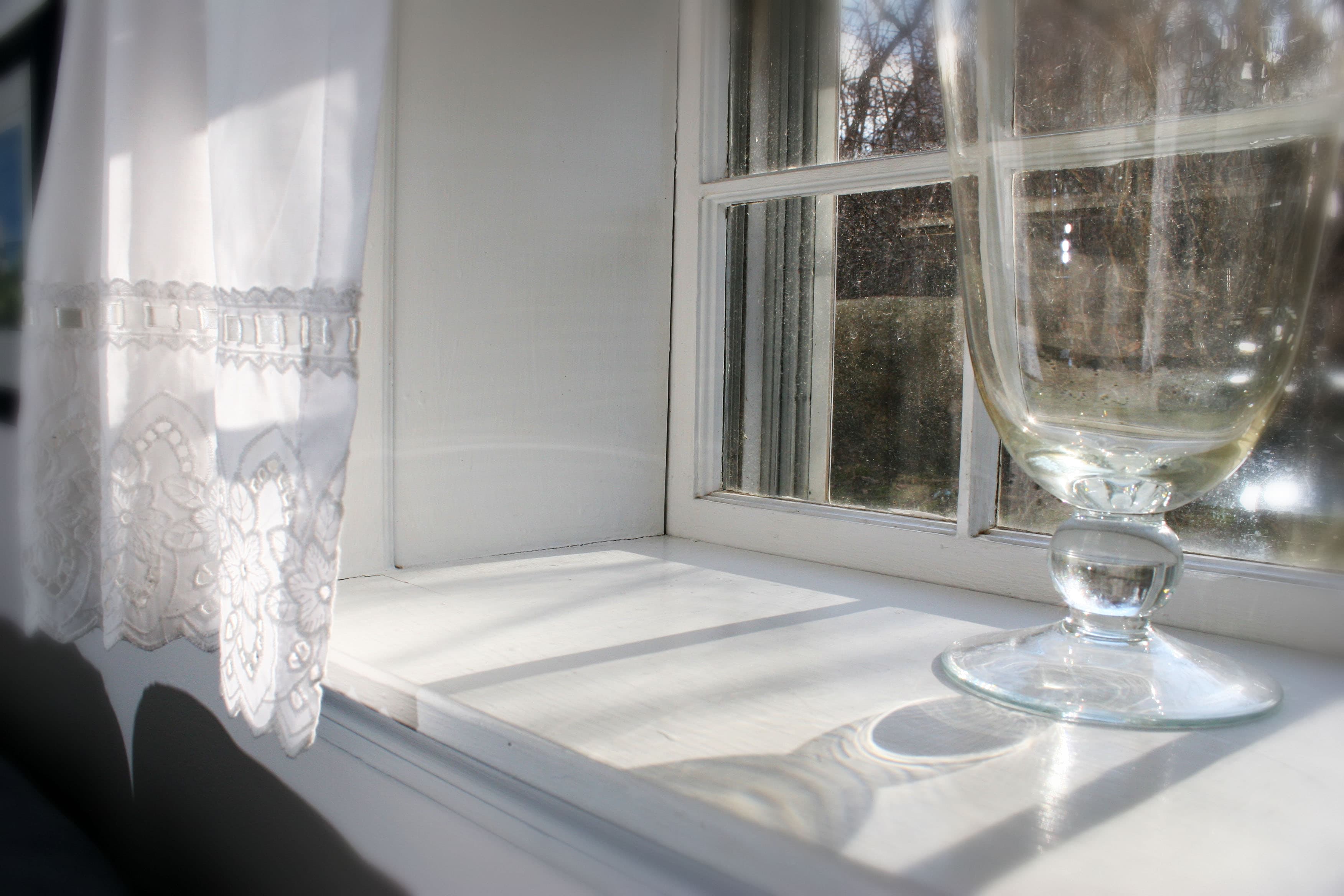 Black and white photo os a window with light streaming into it and a shiny glass vase.