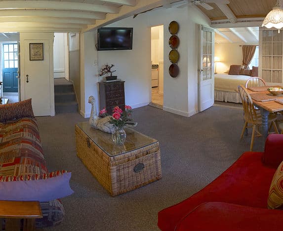 Photo of Lamb's Retreat with wicker table and fresh flowers. There is a maroon chair, partial couch and bedroom in the background