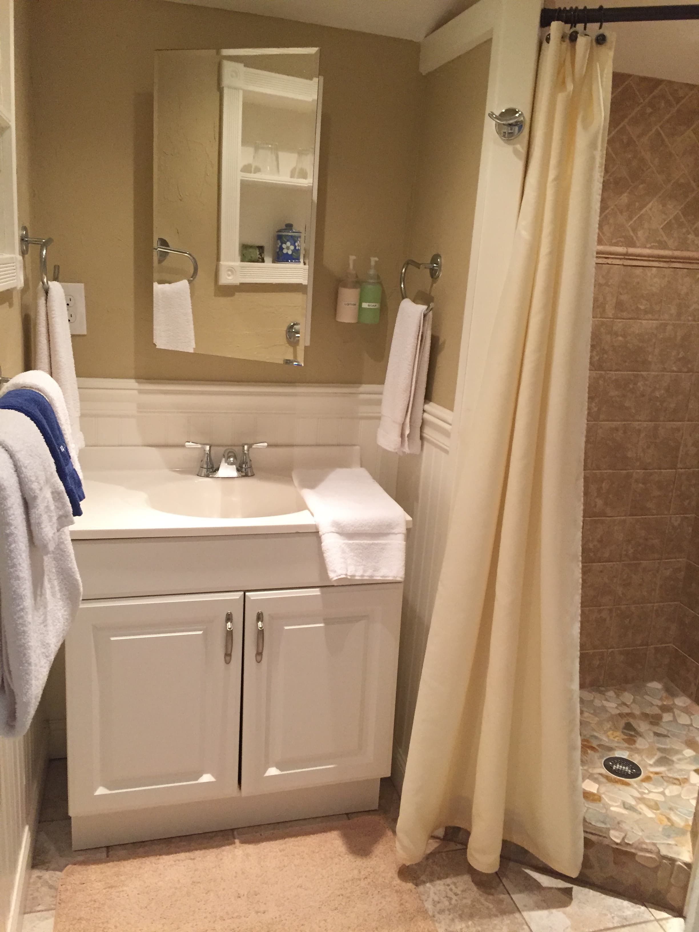 Photo of the bathroom and shower with cream color shower curtain, stone tiling and a medicine cabinet