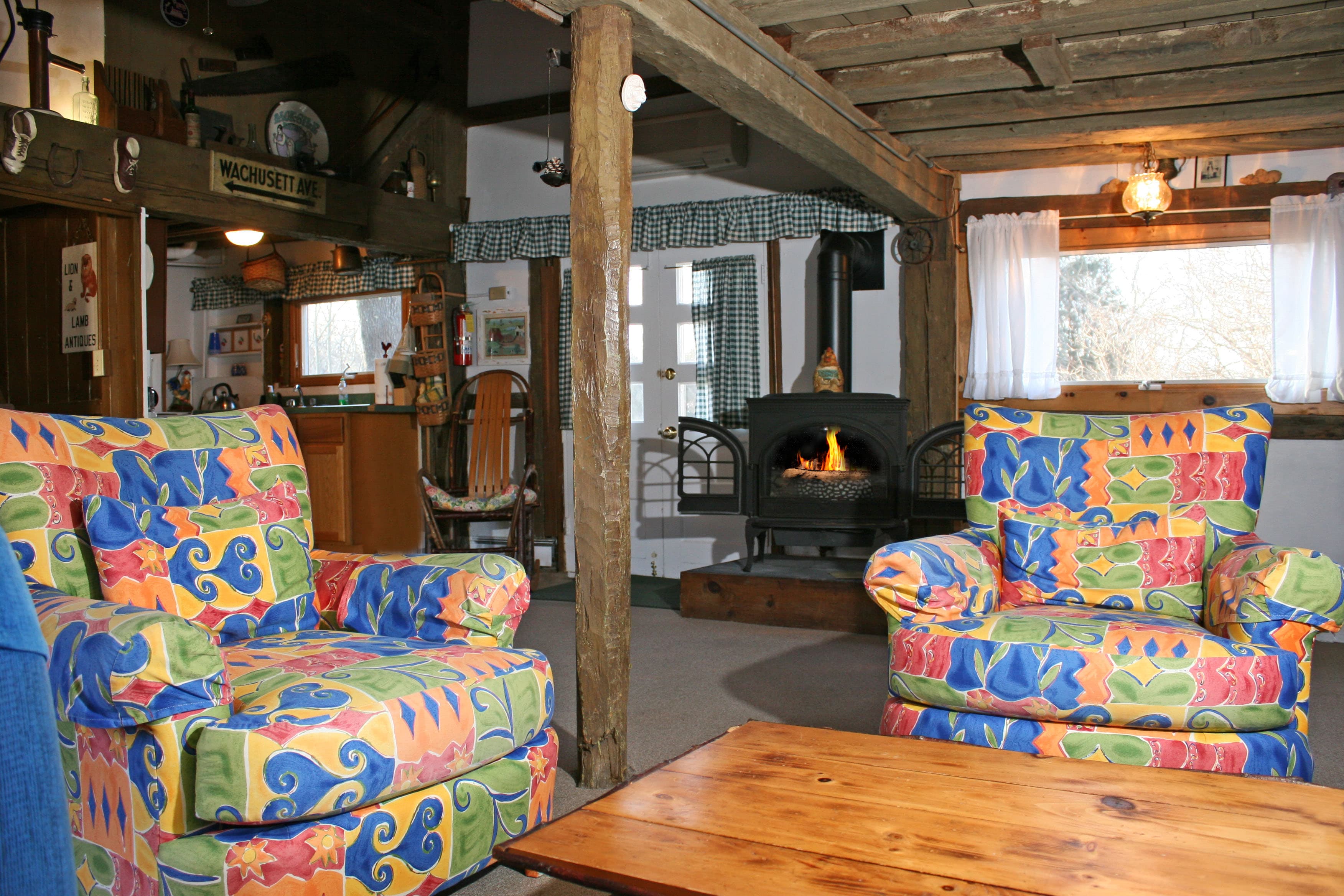 2 multi-colored pattern chairs in front of a wooden coffee table. There is a lit fire in the gas stove behind them