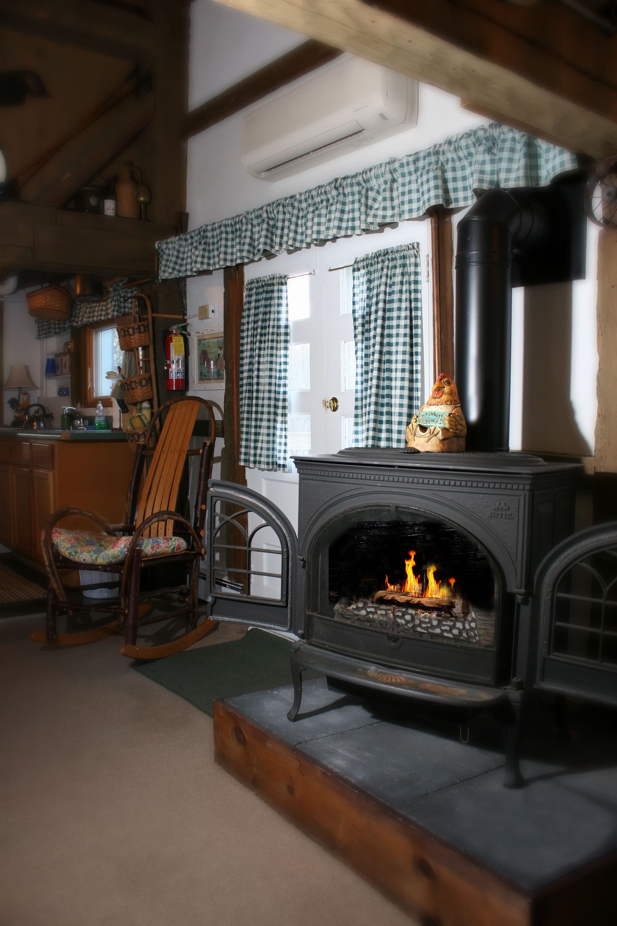 The gas stove has a fire in it with a wooden rocking chair in the background