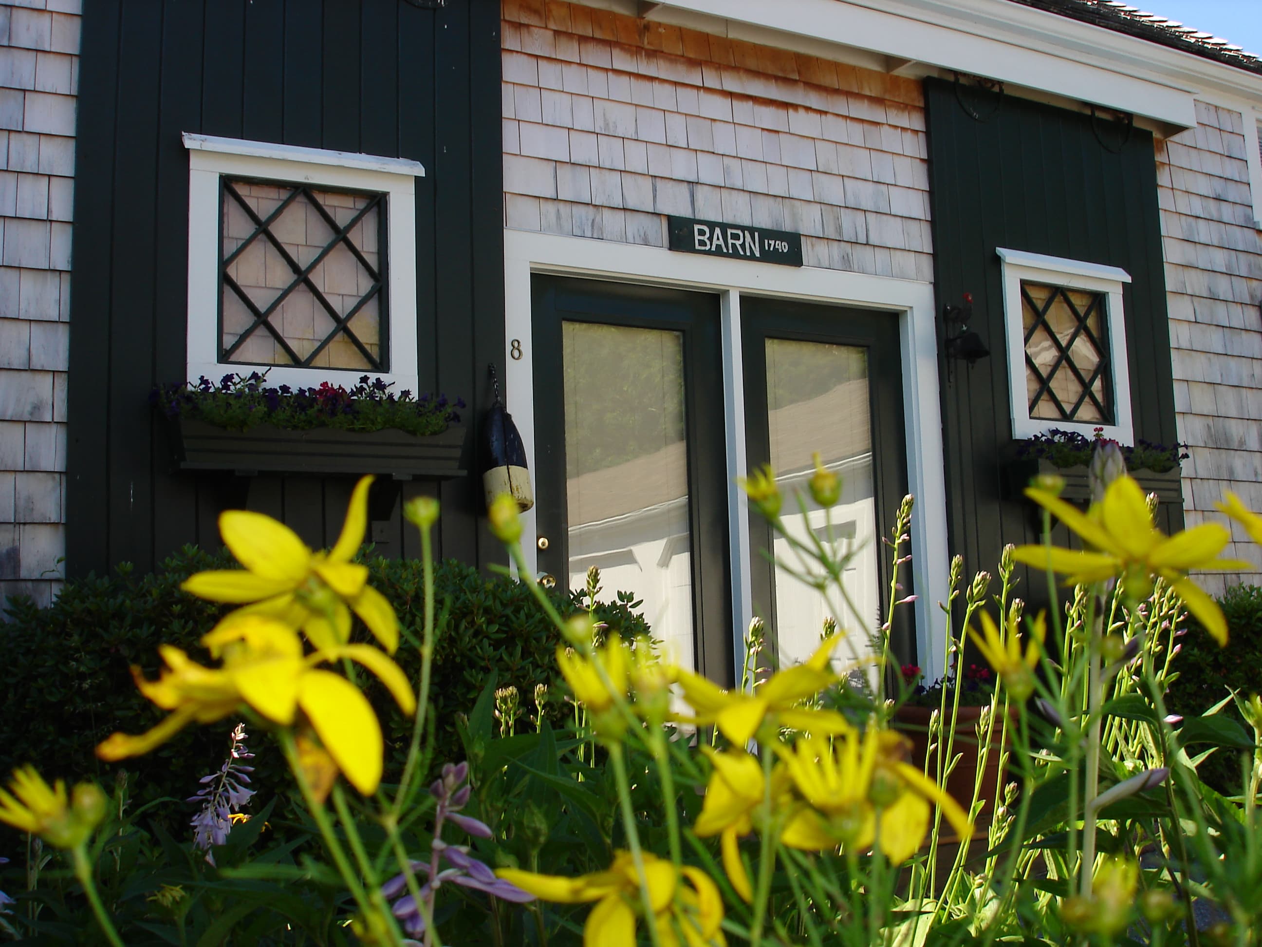 The entrance to the Barn with old green Barn doors with windows and yellow flowers in the foreground. The sign reads 1740 barn