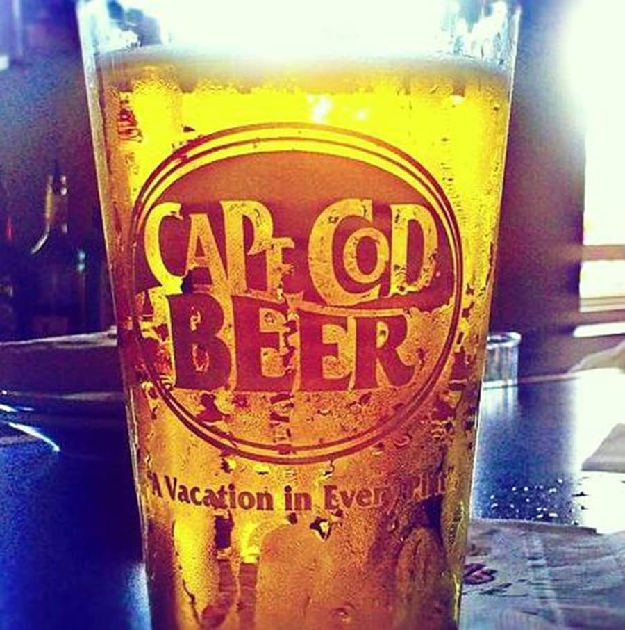 A close-up of a frosty pint glass with the logo "Cape Cod Beer" and a tagline underneath.