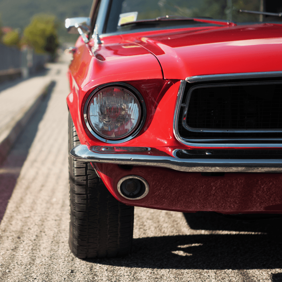 A close-up view of a vintage red car's front bumper and headlights.