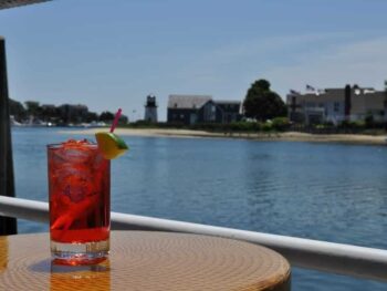 Drink of red liquid with lime set on table in front of river with houses in rear